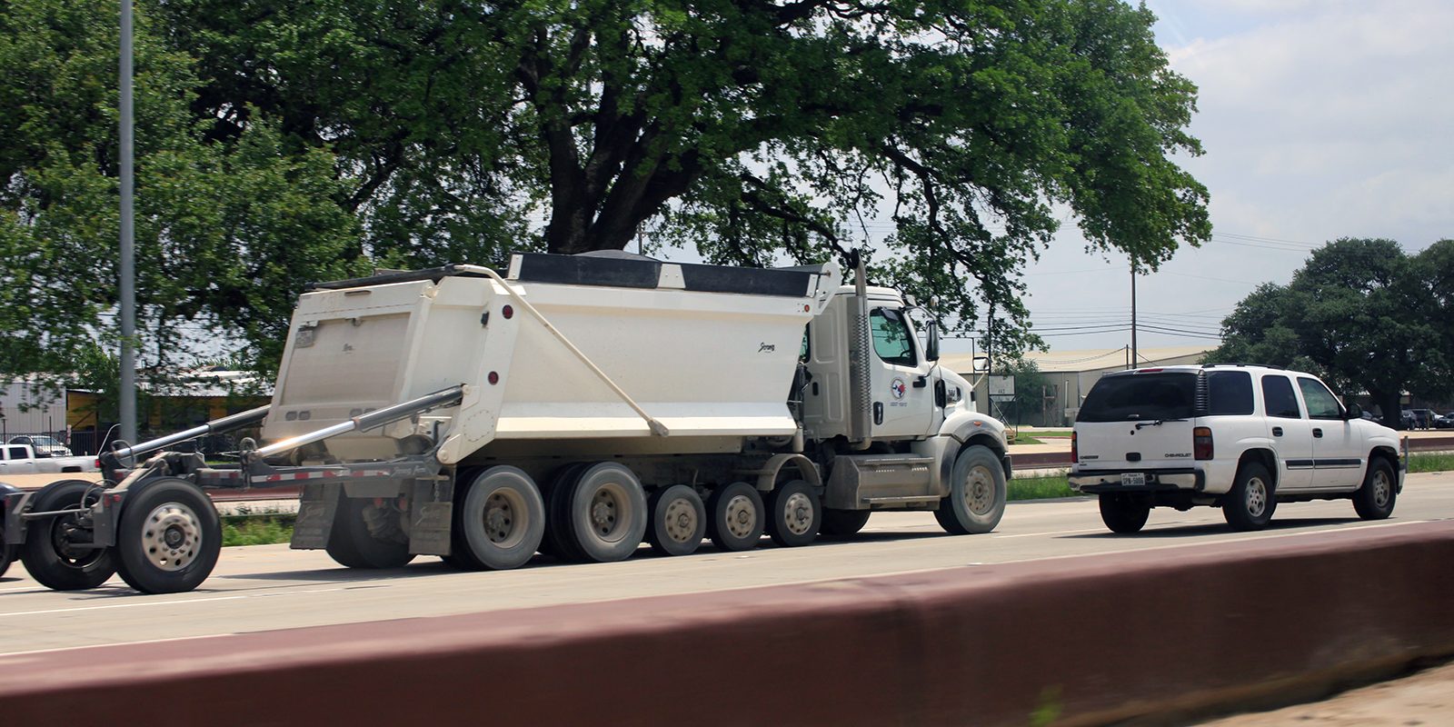 White dump truck hauling material along a highway, the everyday logistics behind large-scale construction