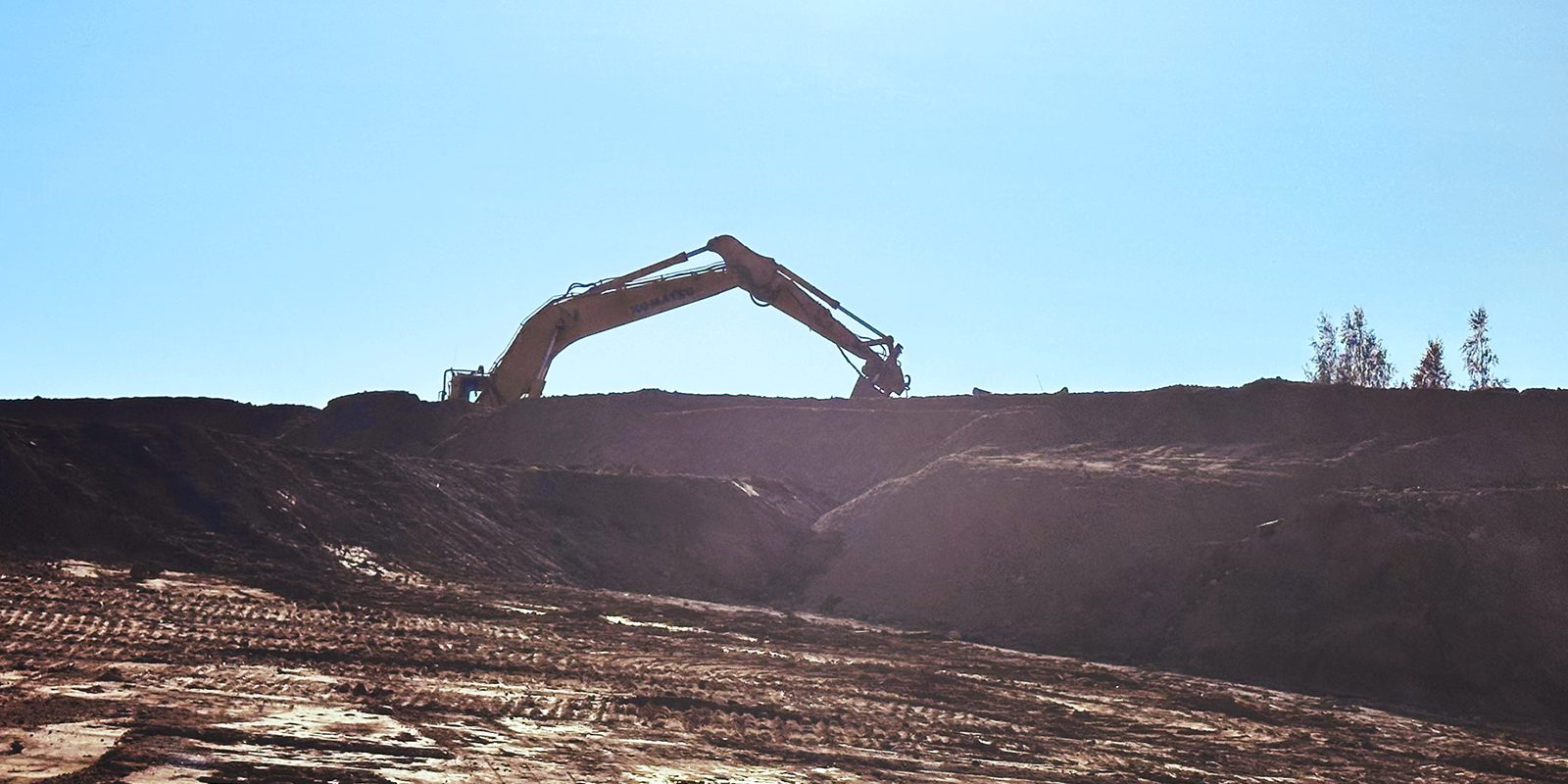 Excavator silhouetted against a clear sky, digging on the ridge of an earthworks embankment