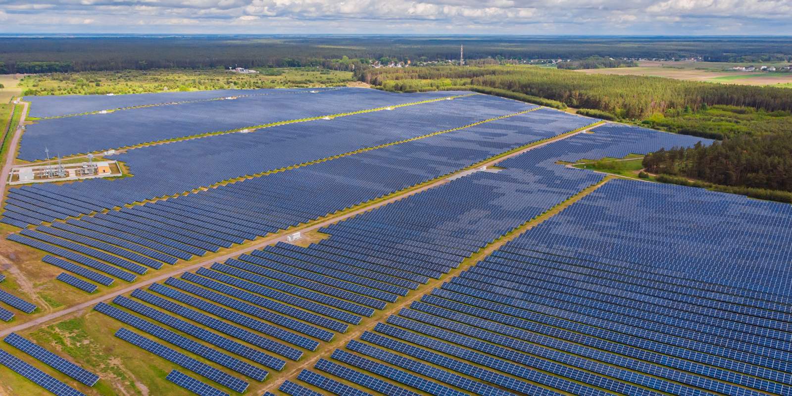 Aerial view of a large solar farm surrounded by fields and forest