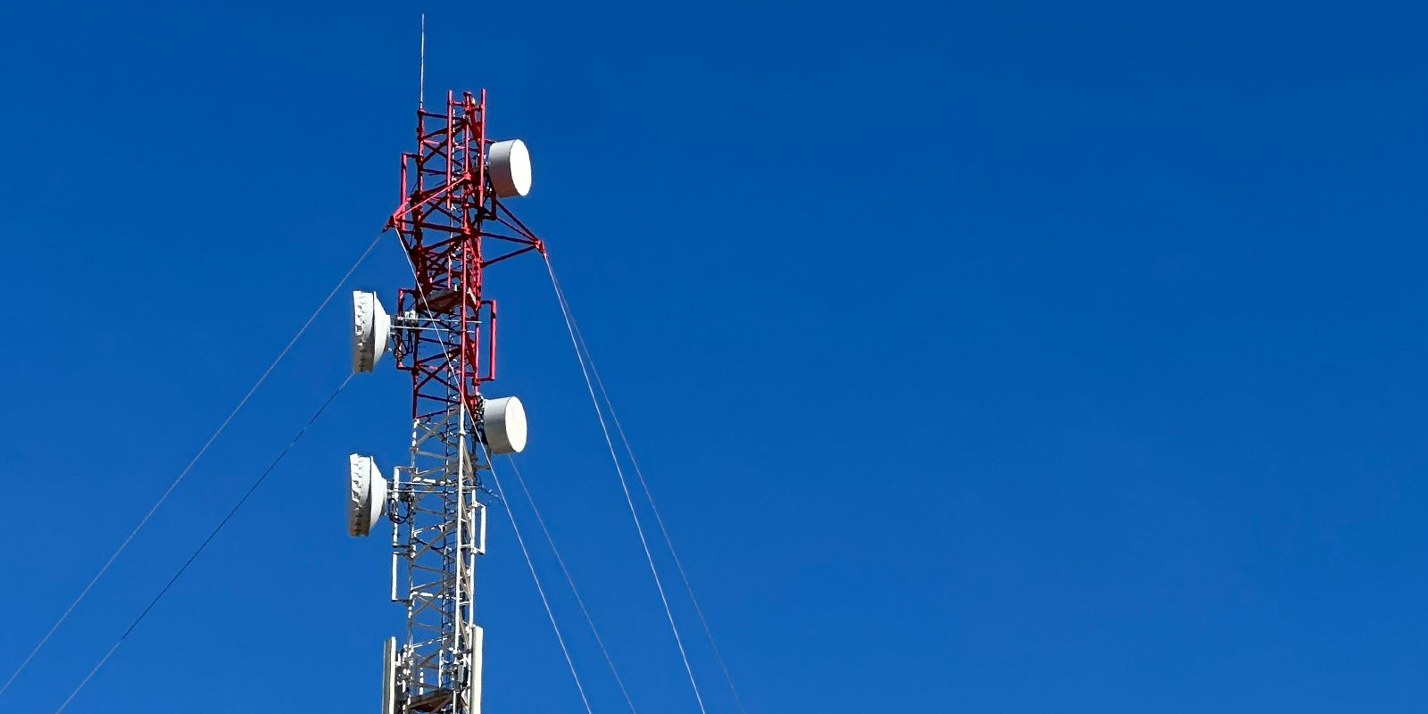 Red-and-white telecommunications mast with panel antennas against a clear blue sky