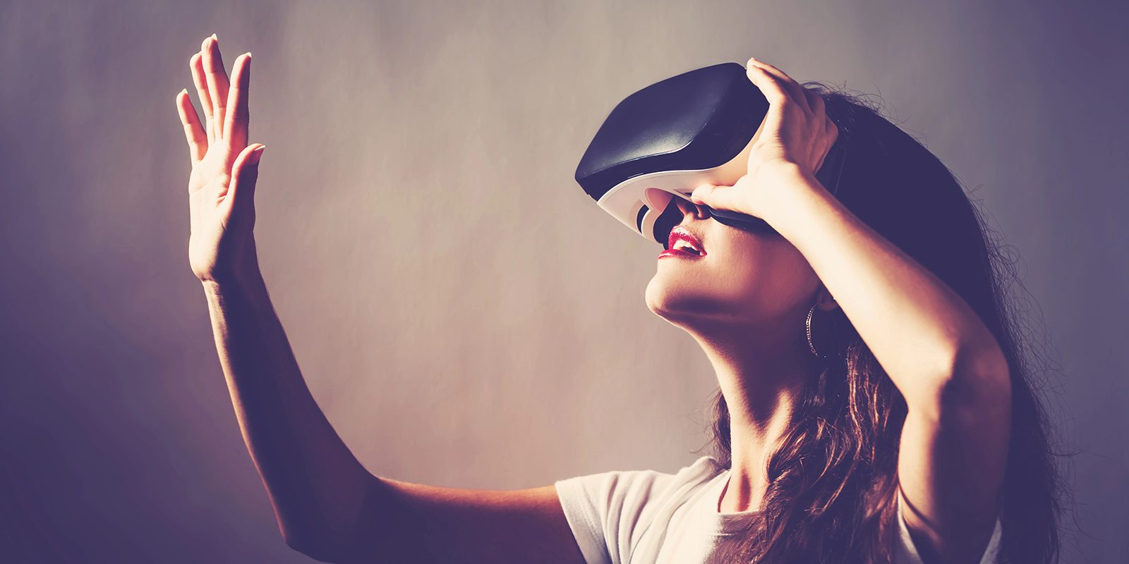 A person in a virtual reality headset, head tilted up, reaching out with one hand toward something only they can see